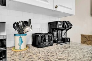 Une cuisine équipée d’un grille-pain, d’une machine à café et d’un porte-ustensiles, le tout posé sur un plan de travail en granit.