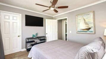Ein Schlafzimmer mit einem Bett, einem Deckenventilator, einem Gemälde und einem Fernseher an der Wand.