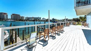 Een houten terras met buitenmeubilair met uitzicht op een jachthaven en stadshemelbeeld.