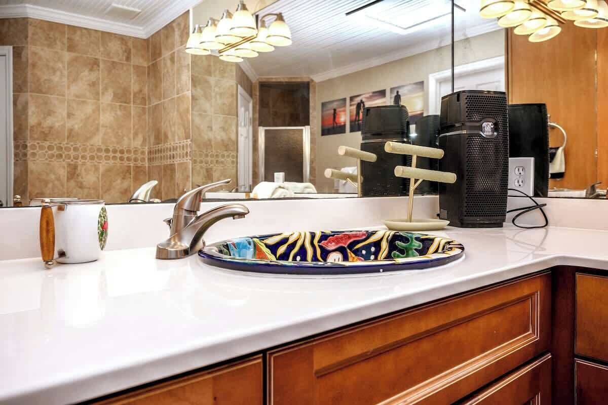 Ein Badezimmer mit einem weißen Waschbecken, einem Spiegel und einem schwarzen Lautsprecher.