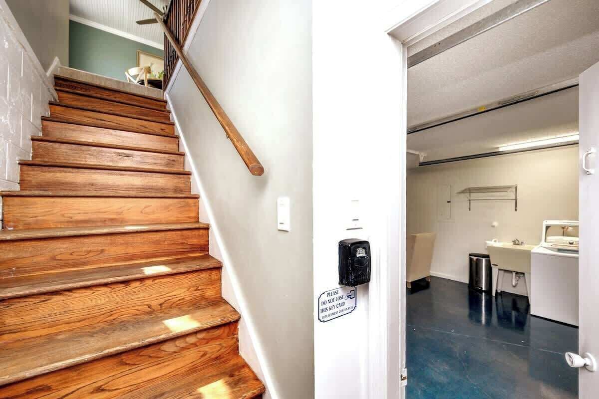 A wooden staircase leading to a room with a white door, a small trash bin, and a sink.