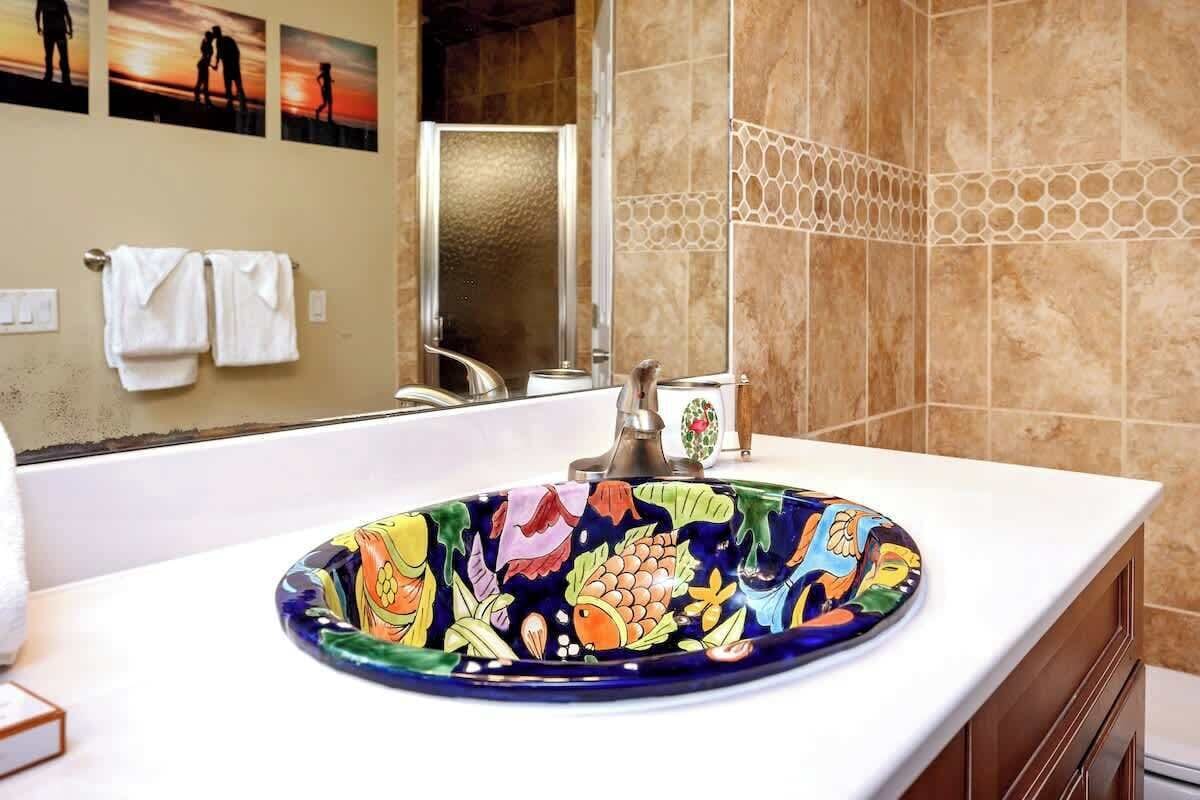 A bathroom with a colorful ceramic sink, a mirror, and a towel rack with towels.