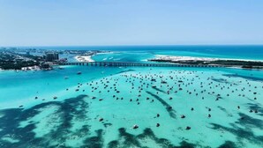 Luchtbeeld van een kustgebied met een grote jachthaven vol boten, een brug en een heldere blauwe zee.