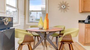 Uma sala de jantar com uma mesa redonda, quatro cadeiras e dois vasos. Há uma janela com vista para edifícios.