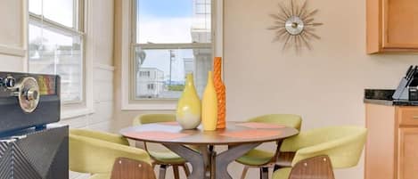 A dining area with a round table, four chairs, and two vases. There is a window with a view of buildings outside.
