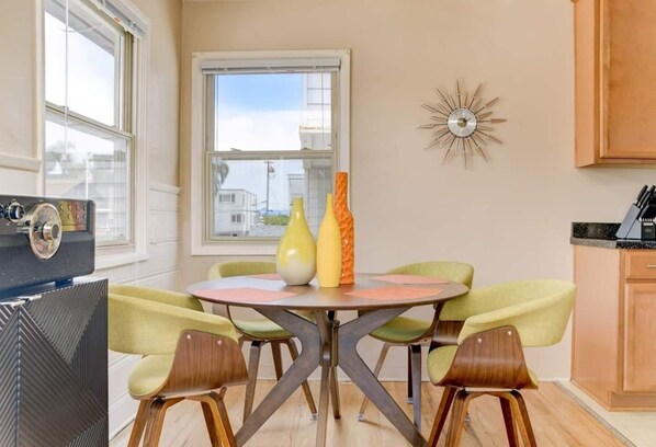 A dining area with a round table, four chairs, and two vases. There is a window with a view of buildings outside.