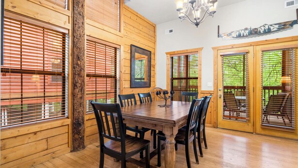 Un comedor con paneles de madera, una mesa grande y sillas, puertas de madera con paneles de vidrio y una araña.