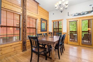 A wooden-paneled dining room with a large table and chairs, wooden doors with glass panels, and a chandelier.