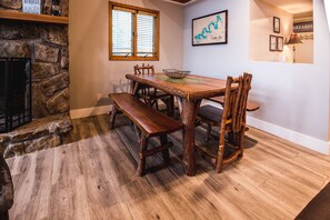 Un coin repas avec une table et des bancs en bois rustique, une cheminée en pierre et une carte accrochée au mur.