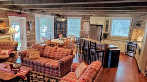 A cozy living room with a fireplace, plaid sofas, a dining table, and a kitchen area with a stove and refrigerator. - The Cozy Canadian Lake House (Dysart et al,)