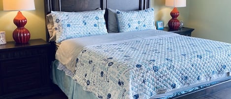 Un dormitorio con cabecera de madera, dos obras de arte enmarcadas sobre la cama y una colcha acolchada con texto.