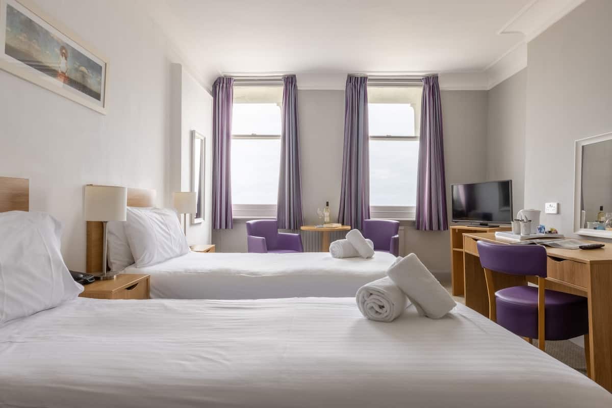 A hotel room with two beds, a desk, a television, and purple chairs.
