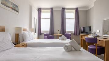 Una habitación de hotel con dos camas, un escritorio, un televisor y sillas moradas.