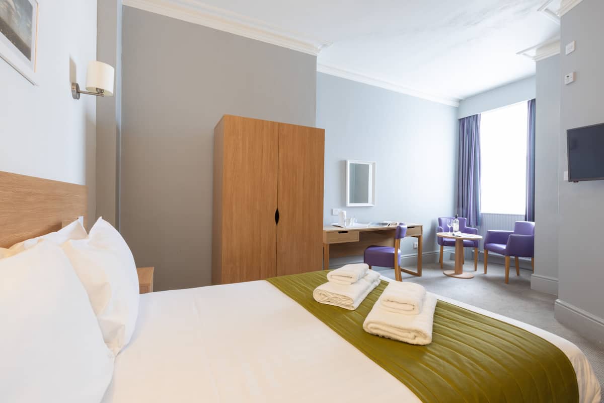 A hotel room with a bed, a desk, a chair, and a wardrobe.