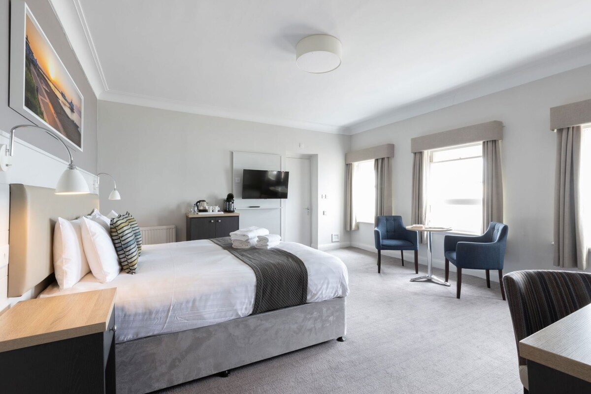 A hotel room with a large bed, a desk, a chair, a TV, and a view of the outdoors.