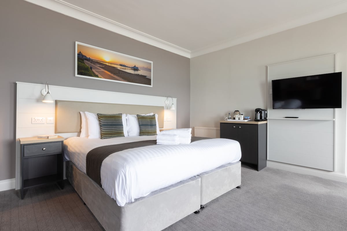 A hotel room with a large bed, a flat-screen TV, a nightstand, a dresser, and a painting on the wall.