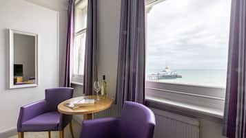 Una habitación con dos sillones morados, una pequeña mesa redonda con un libro y una botella, y vistas a un muelle y al agua.
