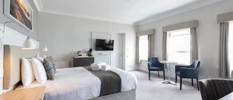 Una habitación de hotel moderna con una cama grande, un escritorio, una silla, un televisor y una ventana con cortinas.
