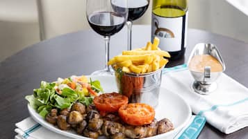 Un plato de comida con ensalada, carne a la parrilla, champiñones y papas fritas, acompañado de una botella de vino y una copa de vino tinto.