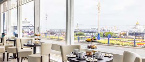 A restaurant with tables set for dining, large windows offering a view of a cityscape and a bridge.