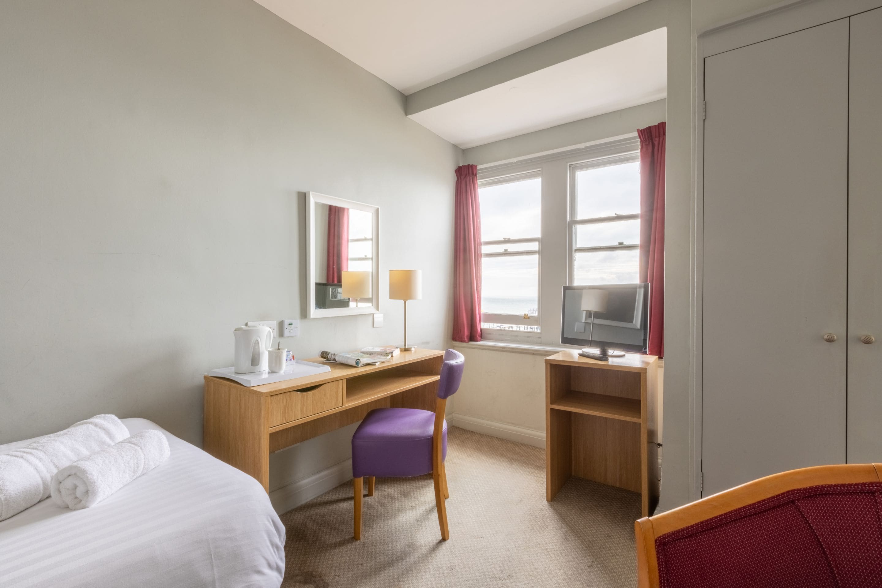 Una habitación de hotel con una cama, un escritorio con computadora, una silla y un televisor.