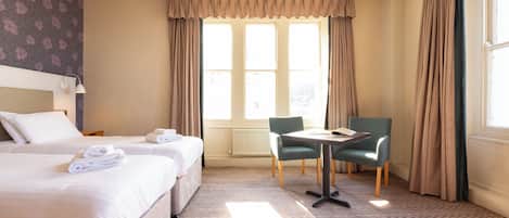 A hotel room with two beds, a dining table, and a chair.