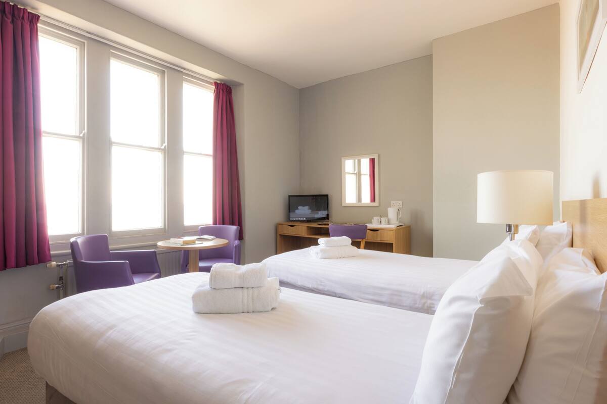 A hotel room with two beds, a desk with a computer, a chair, and a TV.