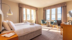 A hotel room with a large bed, two chairs, a desk, and a view of the outdoors. - The Marine Hotel (Llandudno)