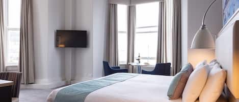 A hotel room with a large bed, a desk, a chair, a TV, and a window with curtains.