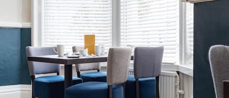 A dining area with a table set for four, featuring blue upholstered chairs and a white tablecloth.