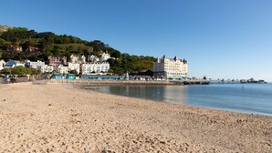 A sandy beach with a row of historic buildings in the background. - The Marine Hotel (Llandudno)
