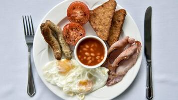 Un plato de comida para el desayuno con huevos, tocino, salchichas, tostadas, tomates y frijoles.