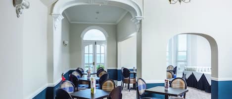 A dining area with tables and chairs, a chandelier, and a view through an arched doorway.