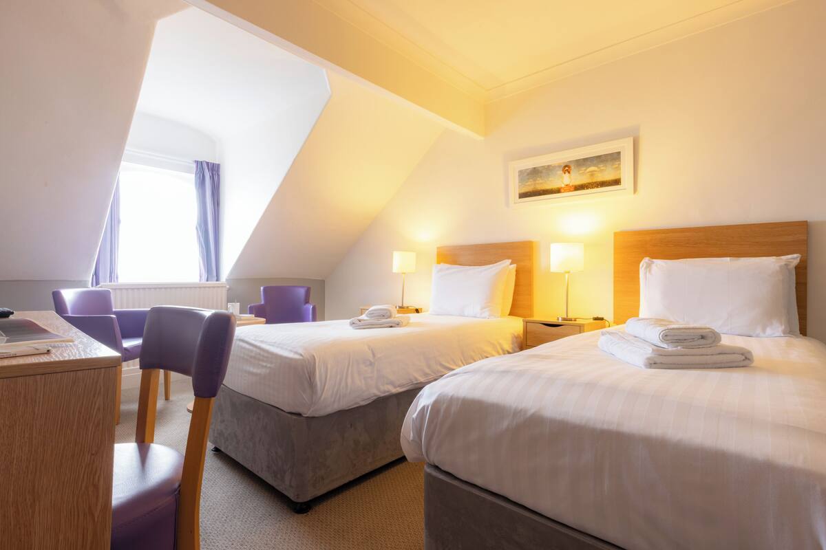 A hotel room with two beds, a desk, and a chair.