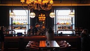 A bar with wooden tables and leather booths, a bartender, and shelves stocked with bottles.