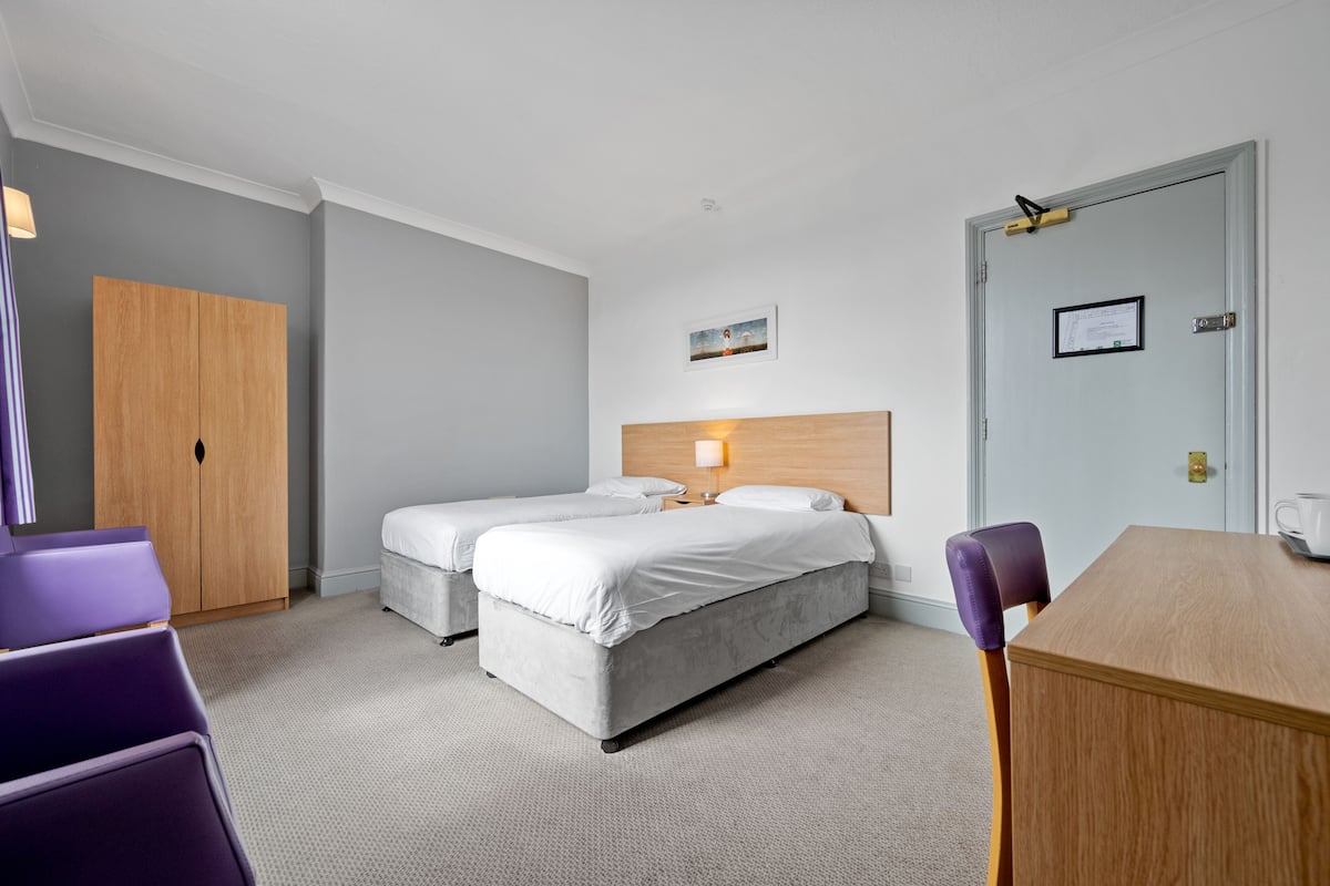 A hotel room with two beds, a wooden wardrobe, a desk, and a chair.