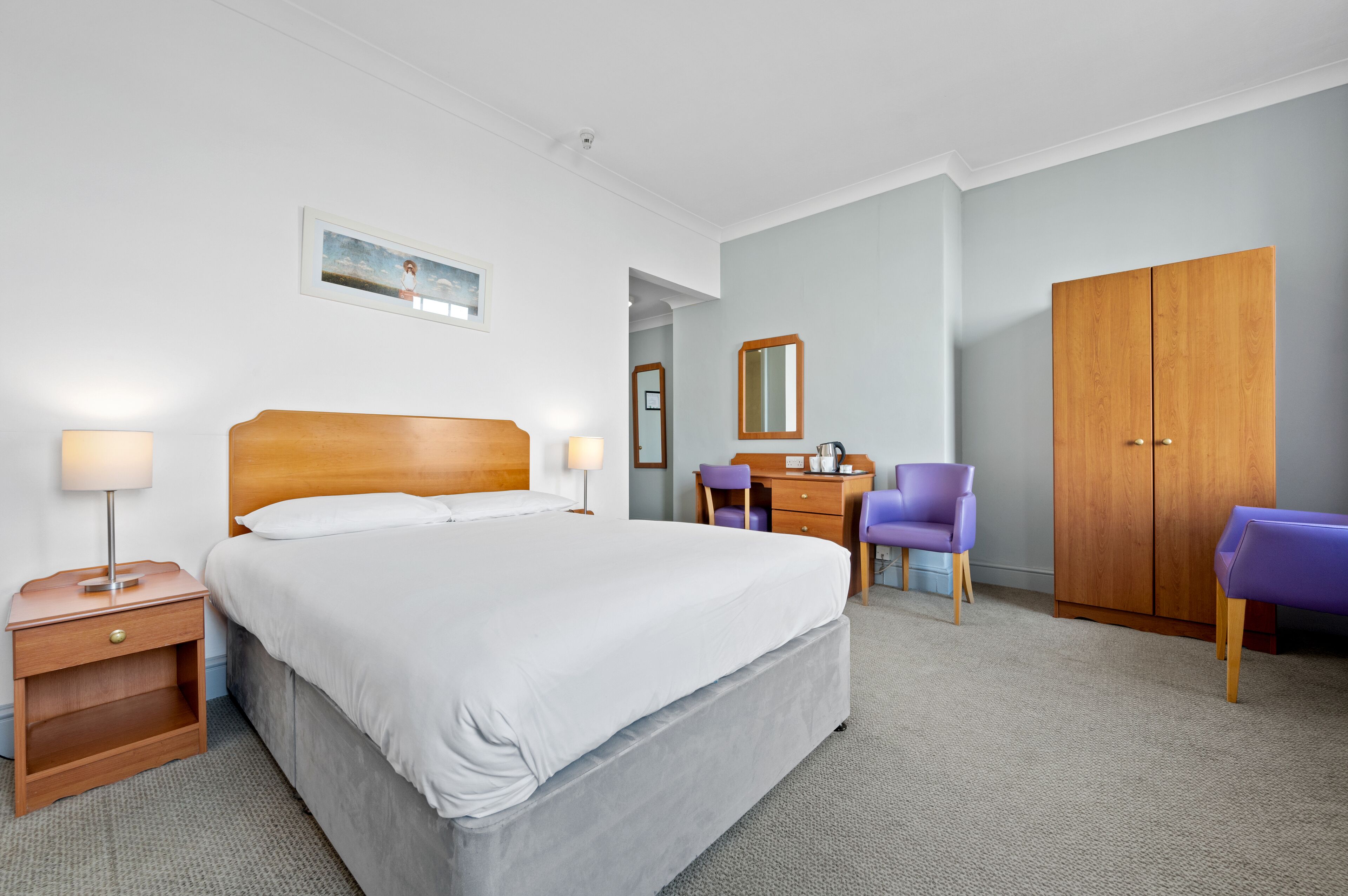 Une chambre d’hôtel avec un grand lit, un bureau, une armoire et une chaise.