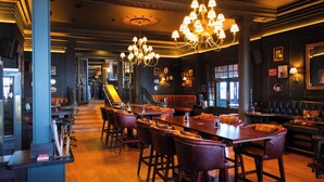 A bar area with wooden flooring, leather bar stools, and a chandelier.