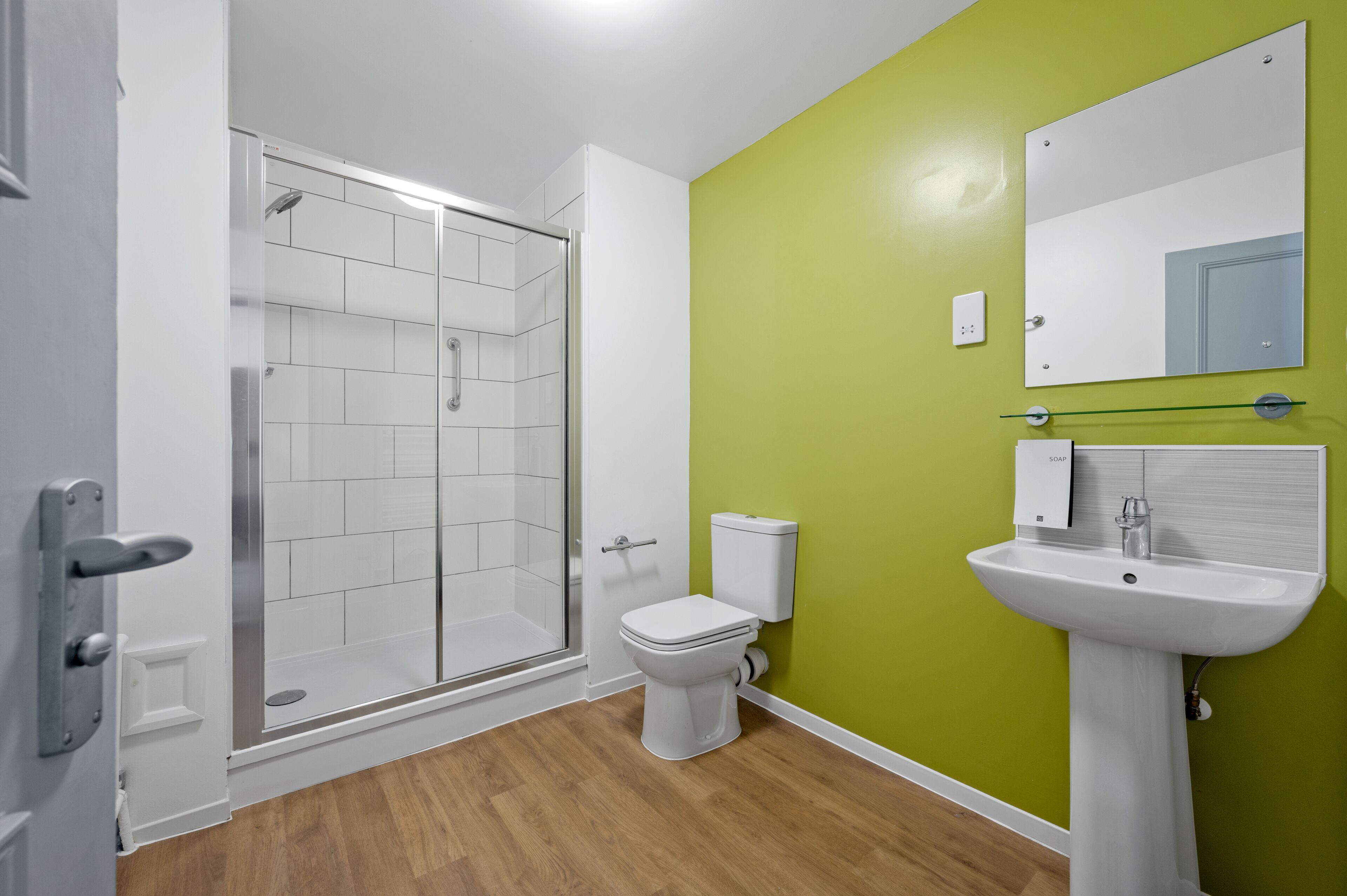 A modern bathroom with a glass shower enclosure, a toilet, and a pedestal sink with a mirror above it.