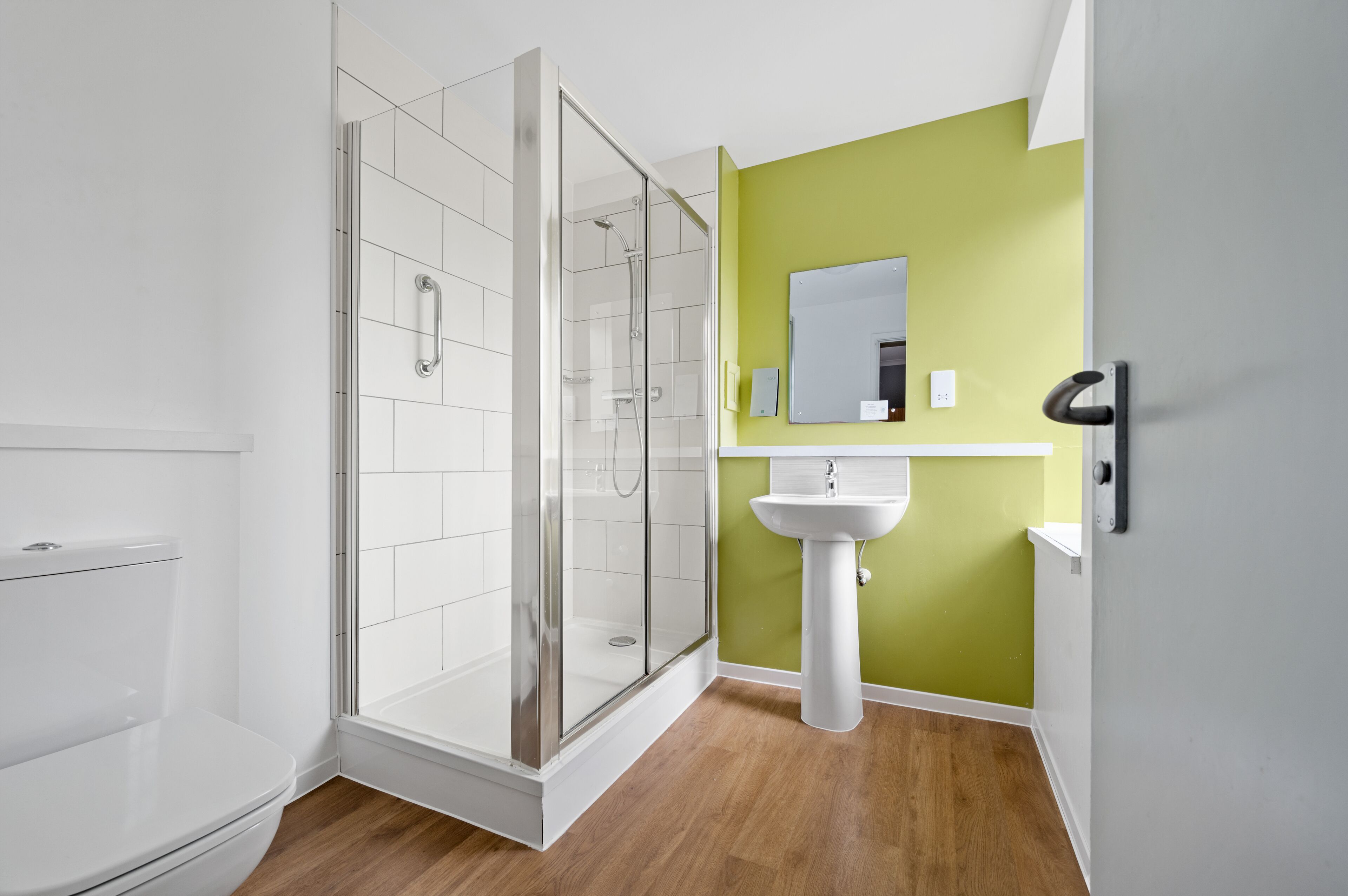 A modern bathroom with a glass-enclosed shower, a white toilet, and a sink against a green wall.