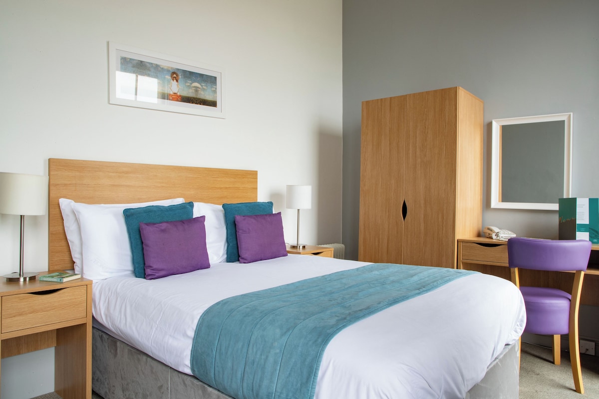A hotel room with a bed, nightstands, a wardrobe, a desk, and a chair.