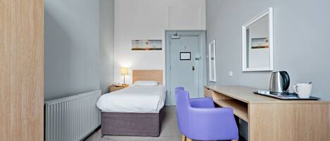 A hotel room with a bed, a desk with a chair, a radiator, and a door.