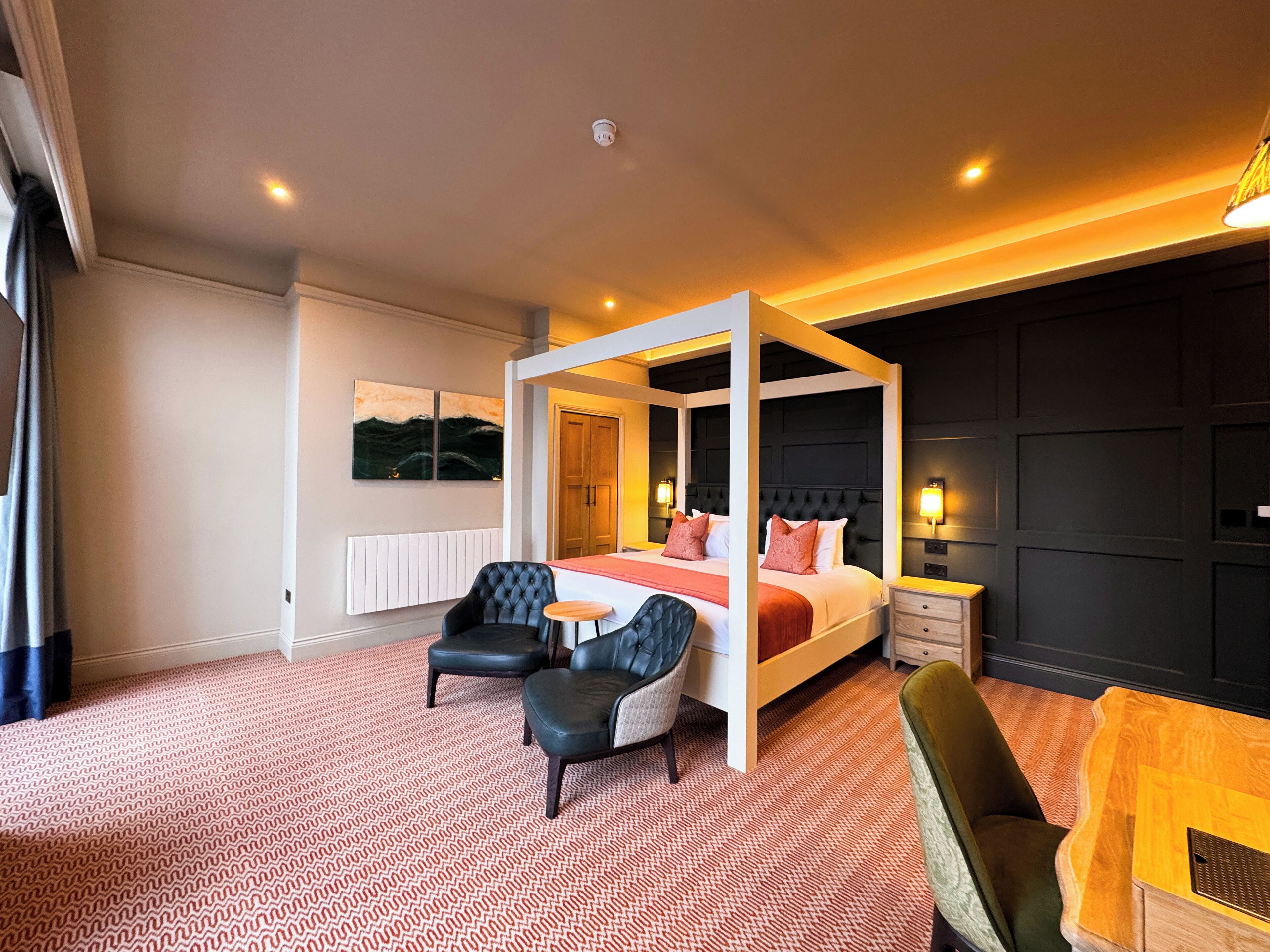 Une chambre d’hôtel moderne avec un lit à baldaquin, deux fauteuils, une petite table et une table de chevet.