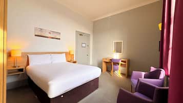 Una habitación de hotel con cama, escritorio, silla, lámpara y puerta.