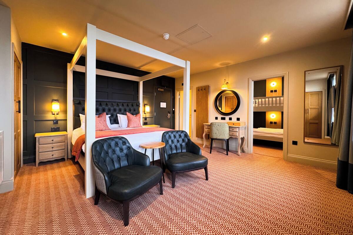 A four-poster bed with a headboard, a desk with a chair, a round mirror, and a wardrobe.