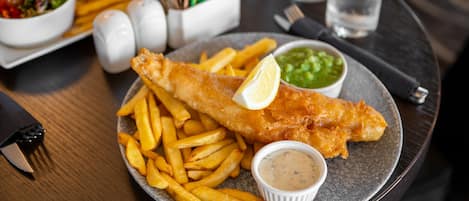 Een bord vis en friet met een partje citroen, tartare saus en erwtjespuree.