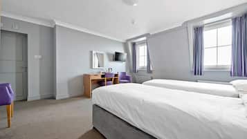 A hotel room with two beds, a desk with a chair, a TV, and a window with curtains.