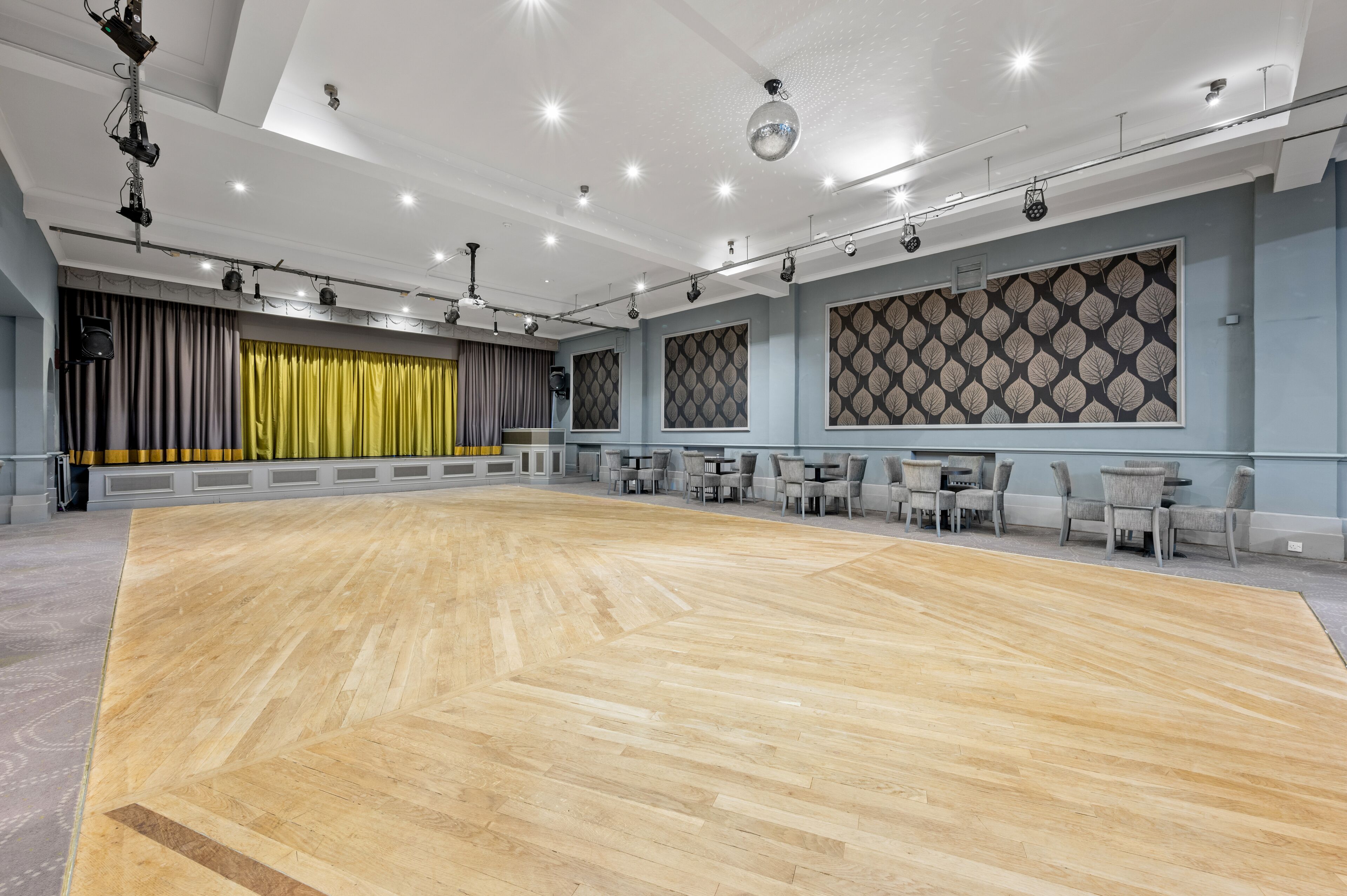 A spacious dance studio with a wooden floor, grey curtains, and a patterned wall.