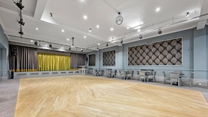 A spacious dance studio with a wooden floor, grey curtains, and a patterned wall.