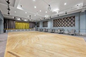 A spacious dance studio with a wooden floor, grey curtains, and a patterned wall.